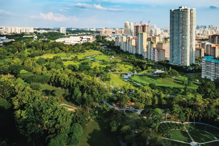 A scenic view of the Bishan neighborhood featuring high-rise HDB blocks, lush greenery, and local residents walking near a community hub known for its diverse food options.