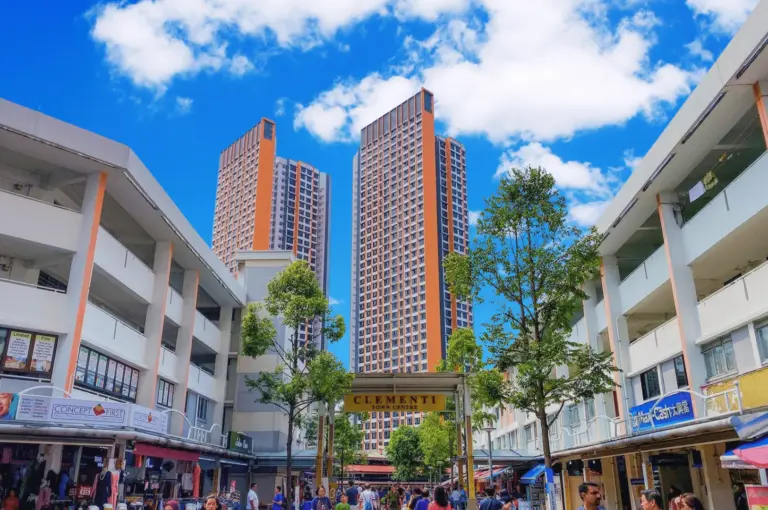 Clementi Town Centre entrance featuring the iconic orange and grey HDB skyscrapers, pedestrian mall with local shops, and a bright cloudy sky.
