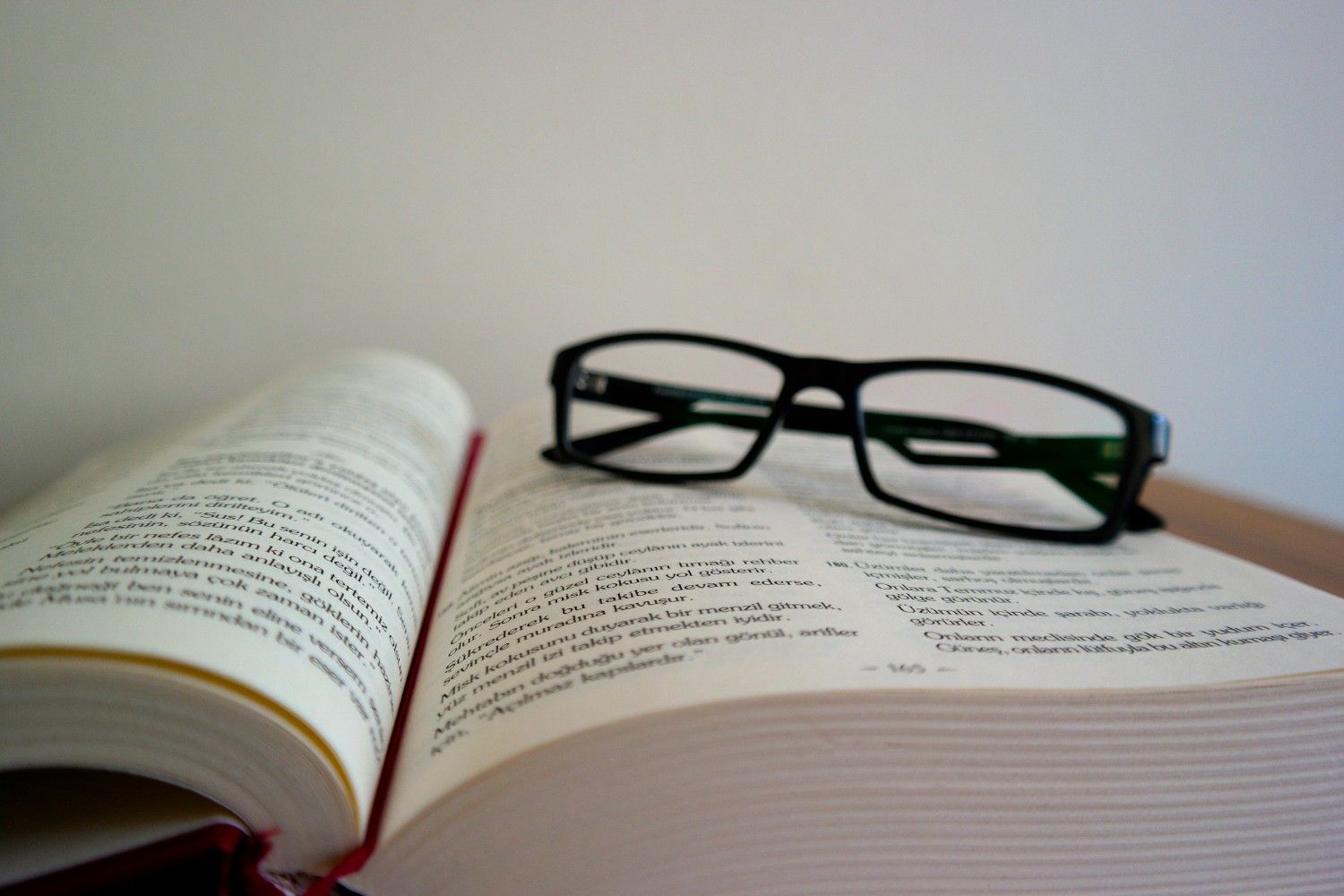 Black-rimmed reading glasses resting on an open book with printed text on a desk.