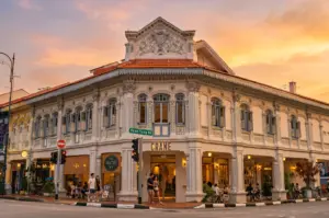 Wide-angle street-level view of a restored heritage shophouse in Singapore housing a modern café, showing the intersection of traditional Peranakan architecture and contemporary dining culture at sunset.