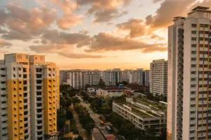 High-angle wide shot of Sembawang residential blocks at sunset, showing public housing towers, surrounding greenery, and neighborhood streets to establish local context.