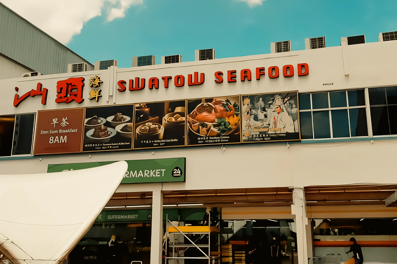 Low-angle exterior shot of Swatow Seafood restaurant signage with bold red Chinese characters and “Swatow Seafood” lettering on a white building facade under a blue sky.