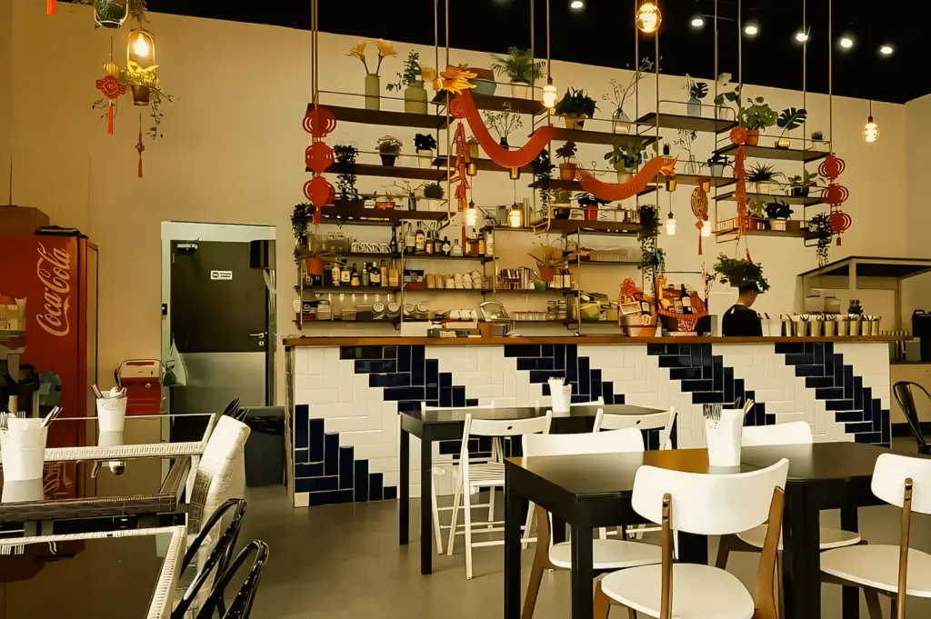 Wide interior shot of Fat Po restaurant showing bar counter seating, hanging decor, potted plants, tiled counter design, and neatly arranged dining tables in a contemporary Asian setting.