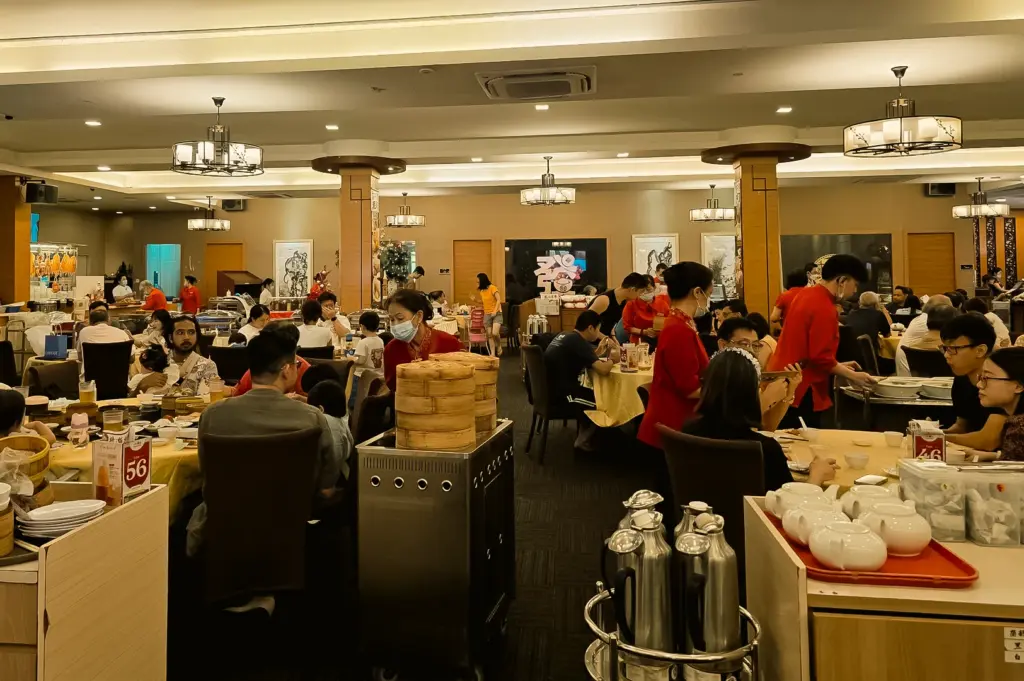 Wide-angle interior shot of Swatow Seafood dining hall showing multiple tables filled with diners, service staff in red uniforms, warm lighting, and traditional Chinese restaurant decor.