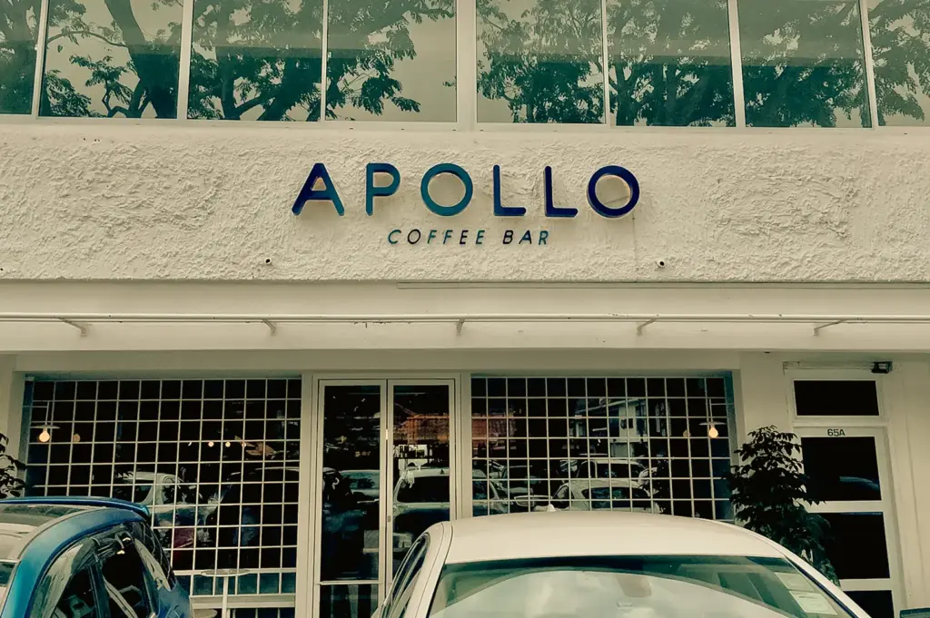 Eye-level straight-on shot of the exterior of Apollo Coffee Bar, featuring a white façade, large windows, and signage above the entrance.