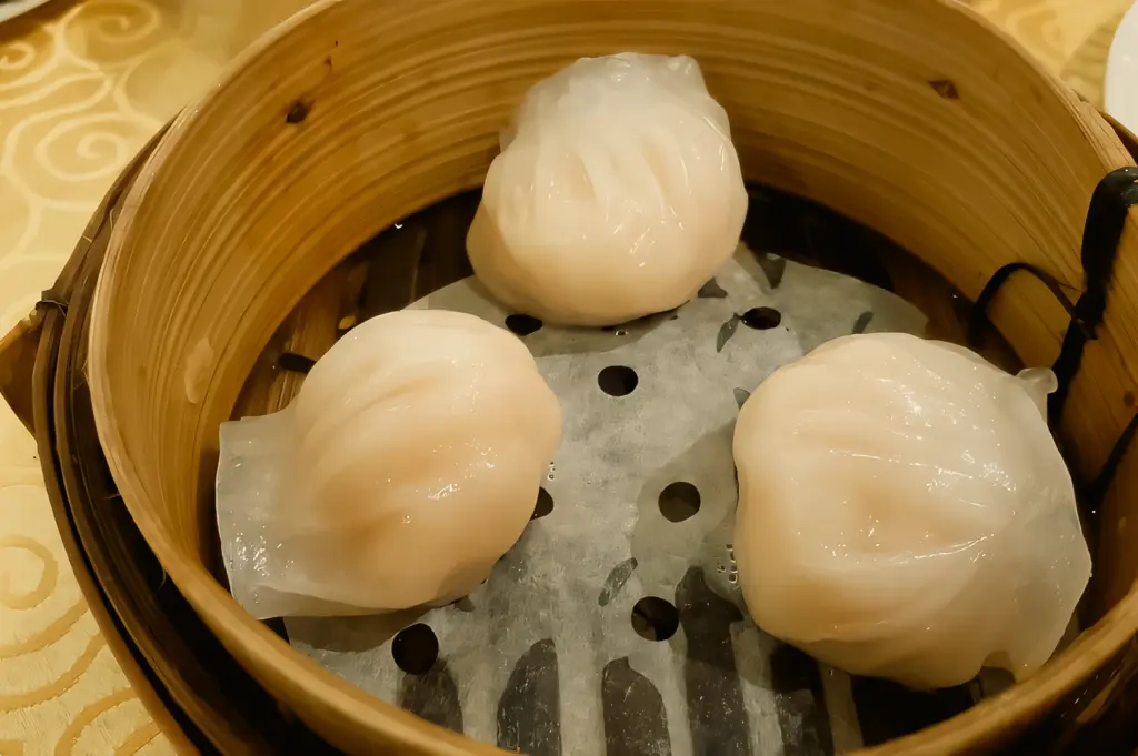 Top-down close-up shot of three translucent steamed shrimp dumplings served in a wooden bamboo dim sum basket.