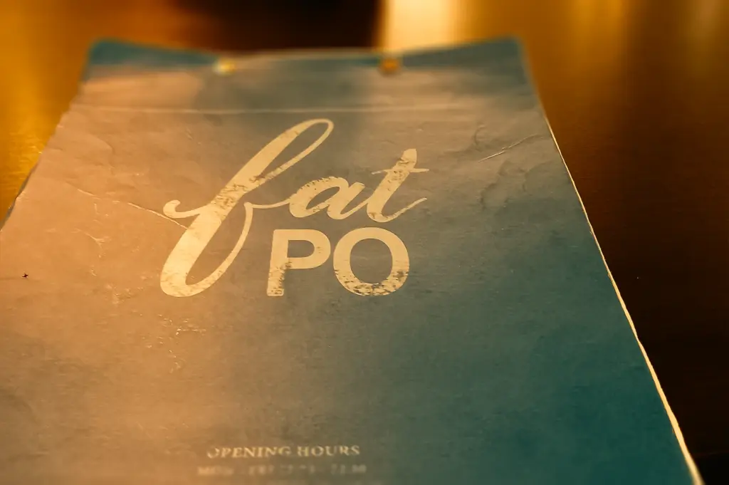 Top-down close-up shot of Fat Po restaurant menu cover featuring minimalist typography on a teal and beige background under warm ambient lighting.