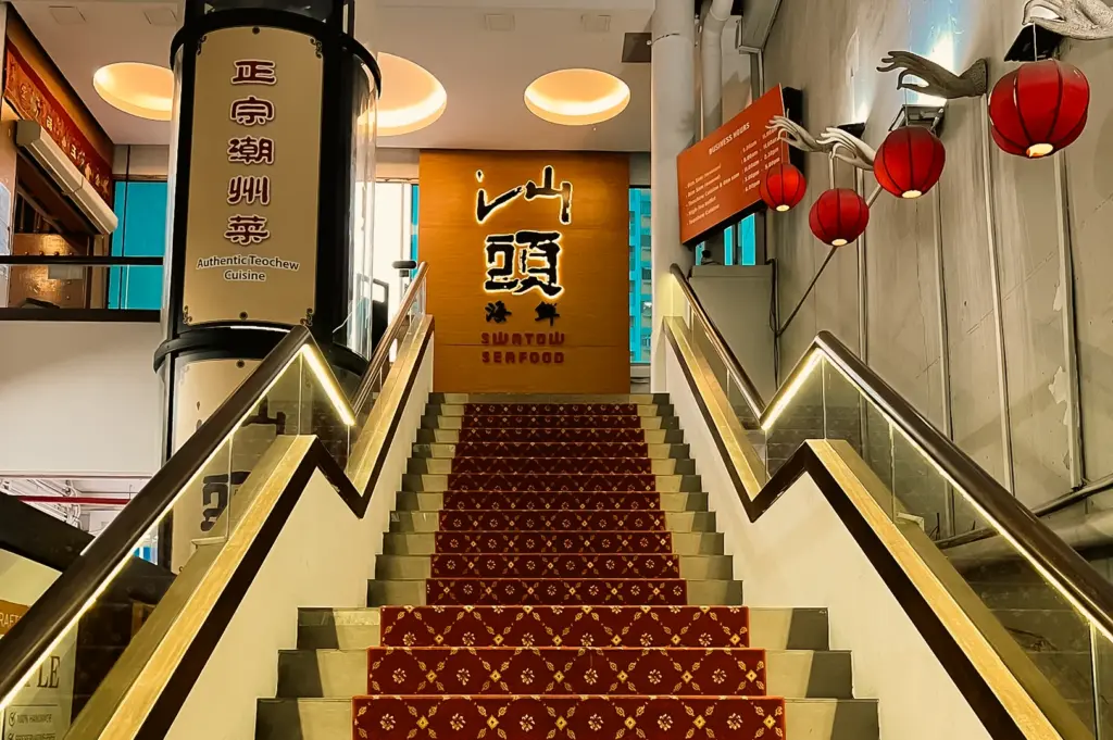 Symmetrical eye-level shot of the Swatow Seafood restaurant entrance featuring a carpeted staircase, illuminated handrails, red lanterns, and branded wall signage.