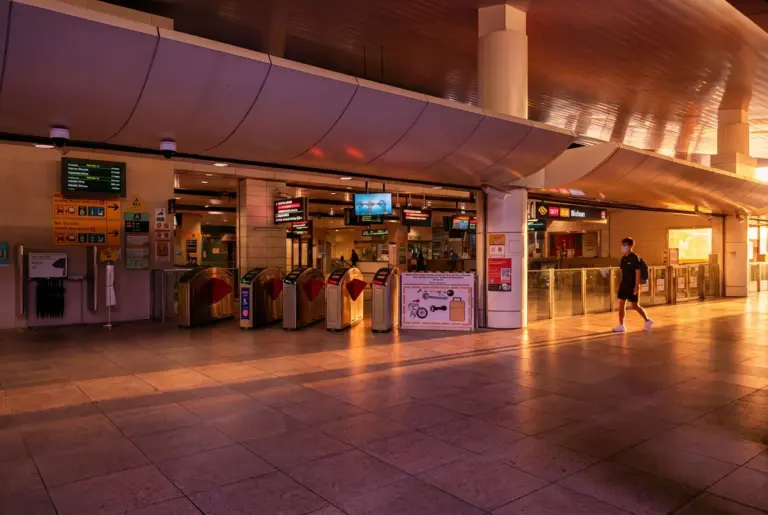 Warm, golden sunset light streaming into the concourse of Bishan MRT station, highlighting the ticketing fare gates and a commuter walking across the tiled floor.