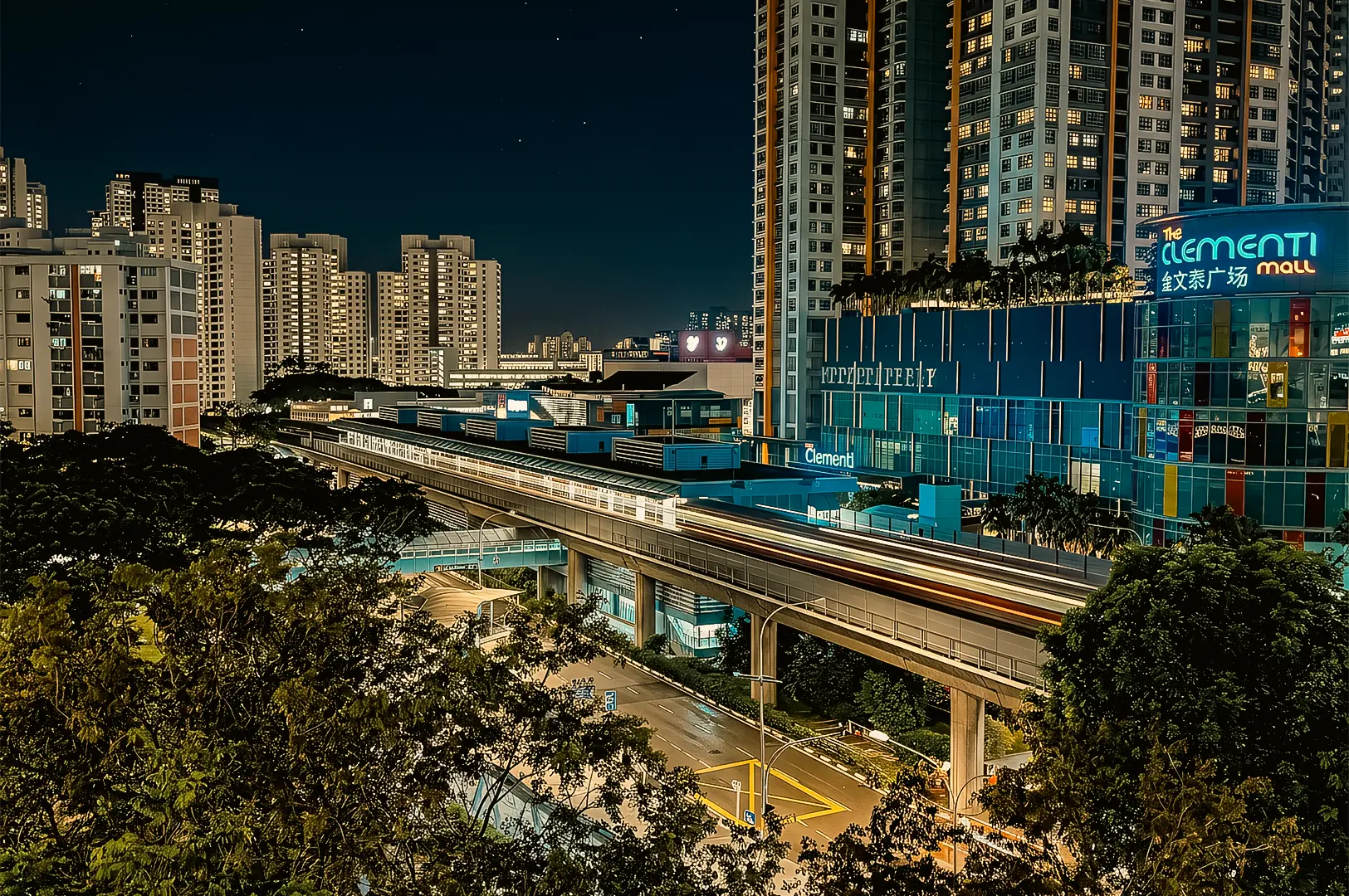Night cityscape of Clementi MRT station and The Clementi Mall in Singapore, featuring elevated train tracks with light trails, surrounded by high-rise residential buildings and urban greenery, captured from a high-angle wide shot