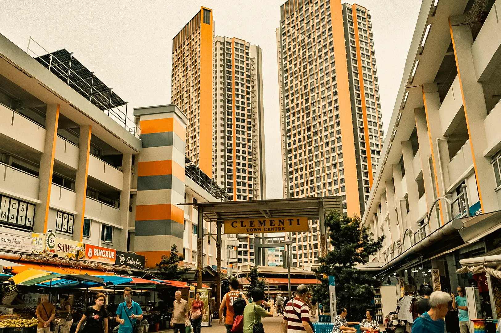 Street-level wide-angle view of Clementi Town Centre in Singapore with bustling hawker stalls, pedestrians, and high-rise HDB flats showcasing local food culture and Nasi Padang heritage
