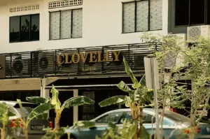 Street-level medium shot of Clovelly Serangoon cafe signage on Jalan Riang surrounded by greenery and residential buildings in Singapore neighborhood