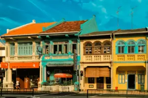 Eye-level street shot of colorful heritage shophouses with pastel facades and traditional architecture under blue sky, showcasing vibrant urban streetscape and cultural dining district.
