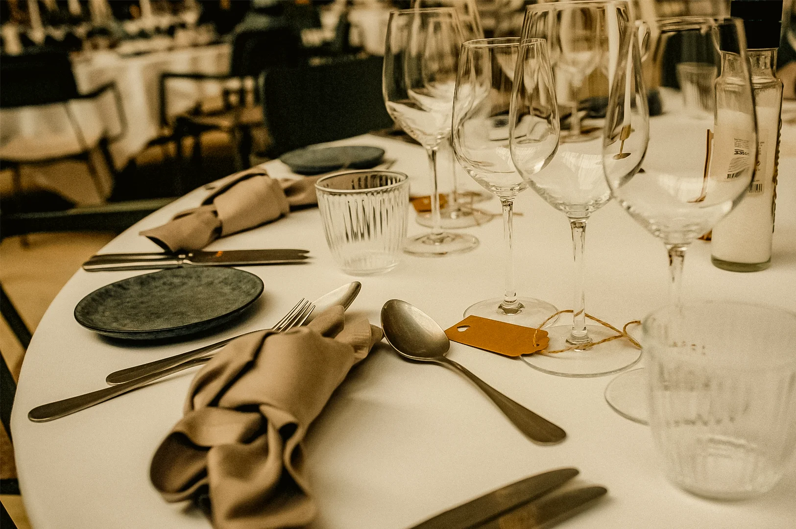 Elegant fine dining table setting with wine glasses, cutlery, and folded napkins in a restaurant, illuminated by warm ambient indoor lighting with soft highlights, captured in a close-up low-angle shot.