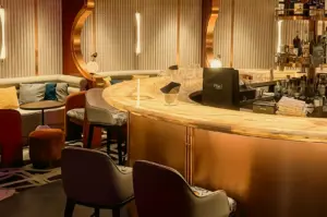 Eye-level wide-angle shot of The Whisper Room Singapore featuring a curved marble cocktail bar, Art Deco gold accents, plush lounge seating, and warm ambient lighting in an elegant nightlife setting