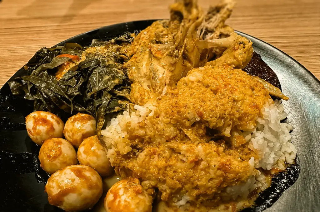 Close-up angled shot of Nasi Padang plate with rice, ayam curry in rich coconut gravy, sambal eggs, and leafy vegetables highlighting traditional Minangkabau flavors in Clementi Singapore