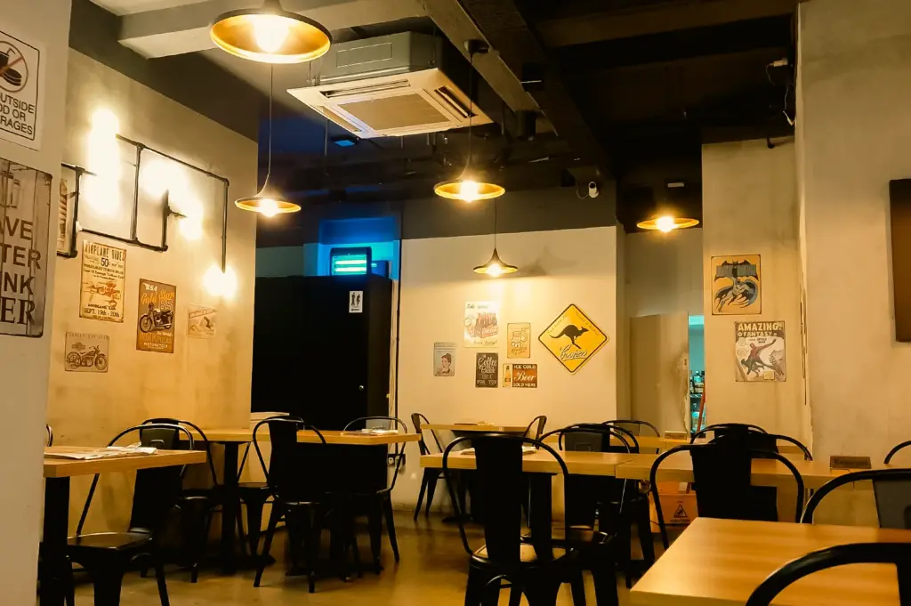 Cozy industrial-style interior of The Larder Cafe featuring wooden tables, vintage wall art, and warm pendant lights, captured in a wide-angle eye-level shot showcasing the spacious dining ambiance.