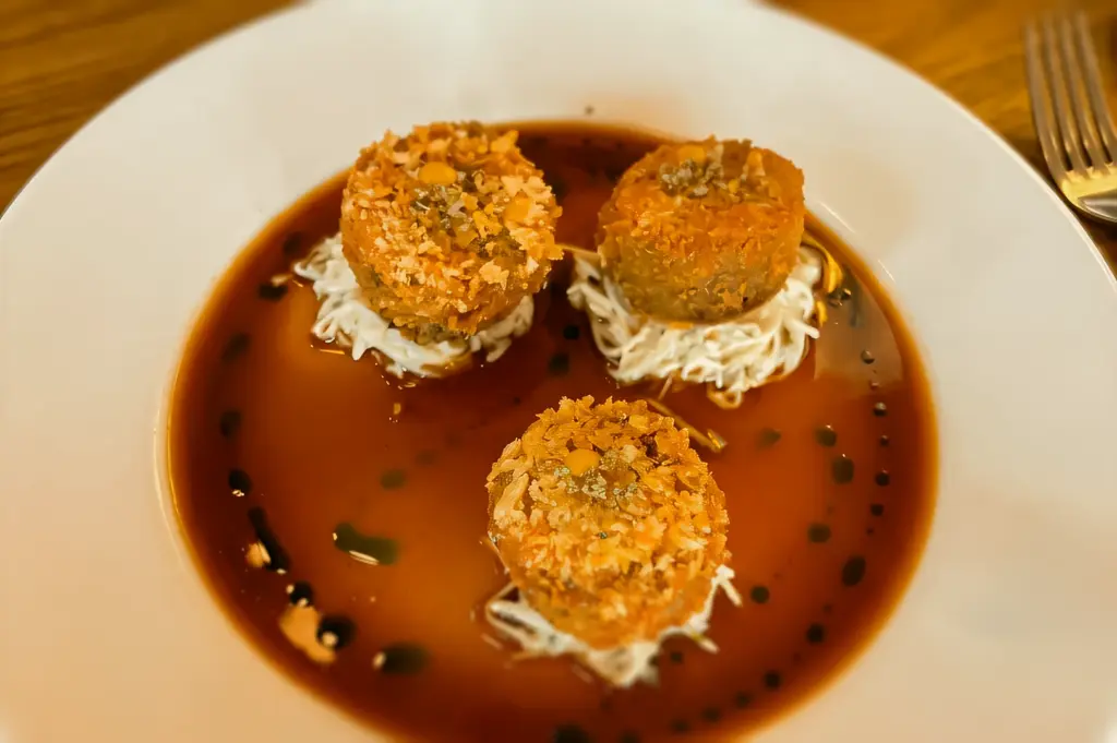 Top-down close-up shot of truffle croquettes appetizer plated in rich sauce at The Whisper Room Singapore, showcasing elevated bar snacks and fine dining presentation