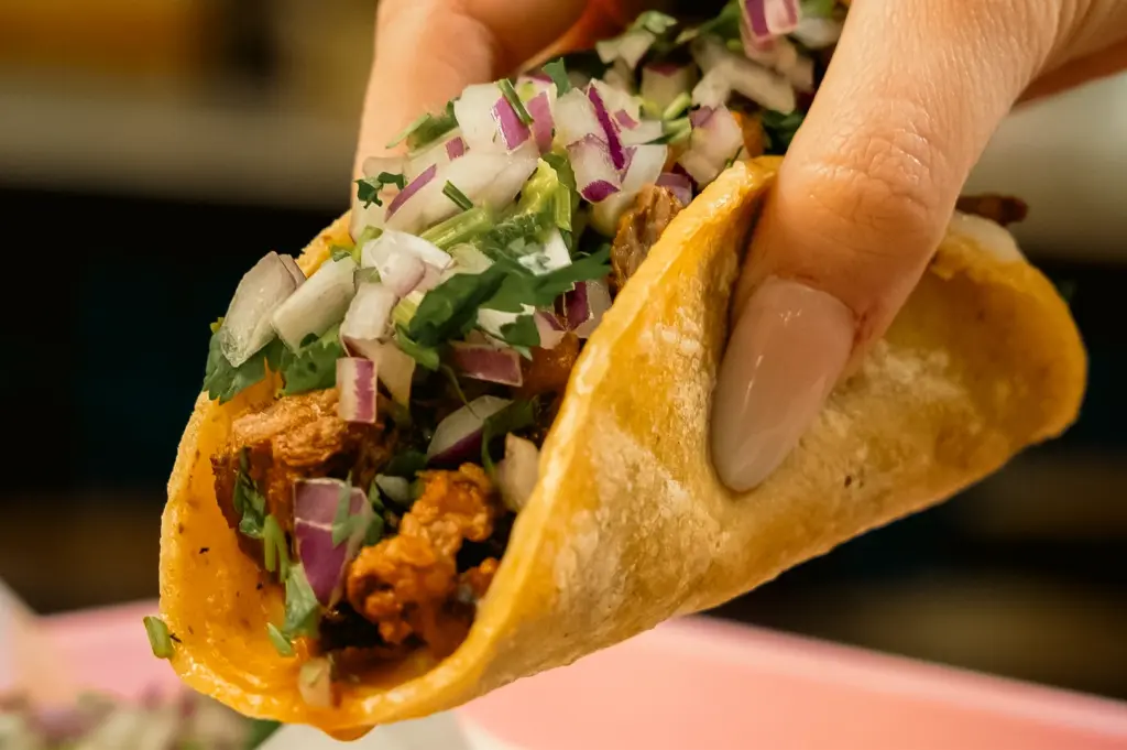 Extreme close-up of street taco in soft corn tortilla filled with seasoned meat, diced onions, and cilantro, handheld for quick bite lunch, bold street food tacos Singapore