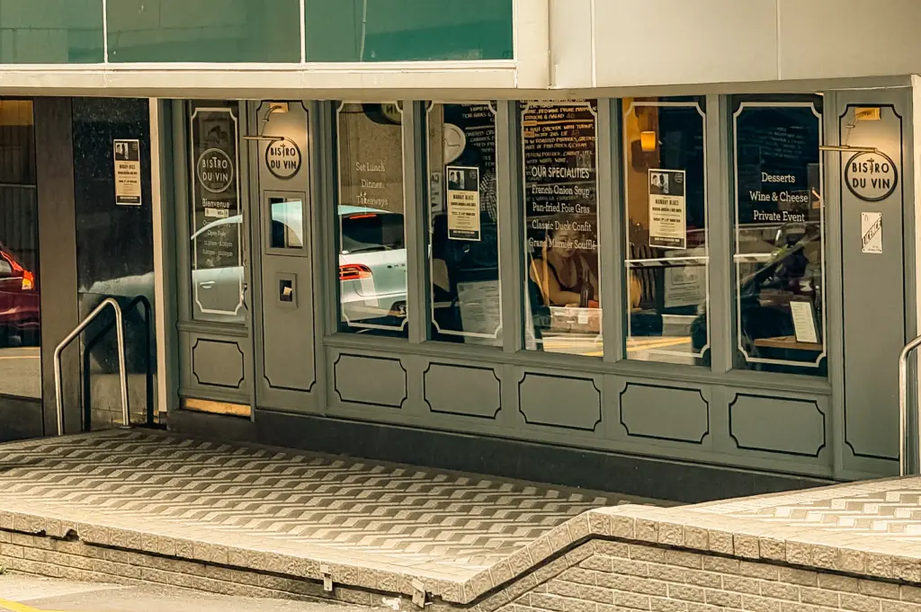 Bistro du Vin storefront with classic signage and window display, illuminated by soft natural daylight and subtle interior lighting glow, captured in a straight-on street-level shot.