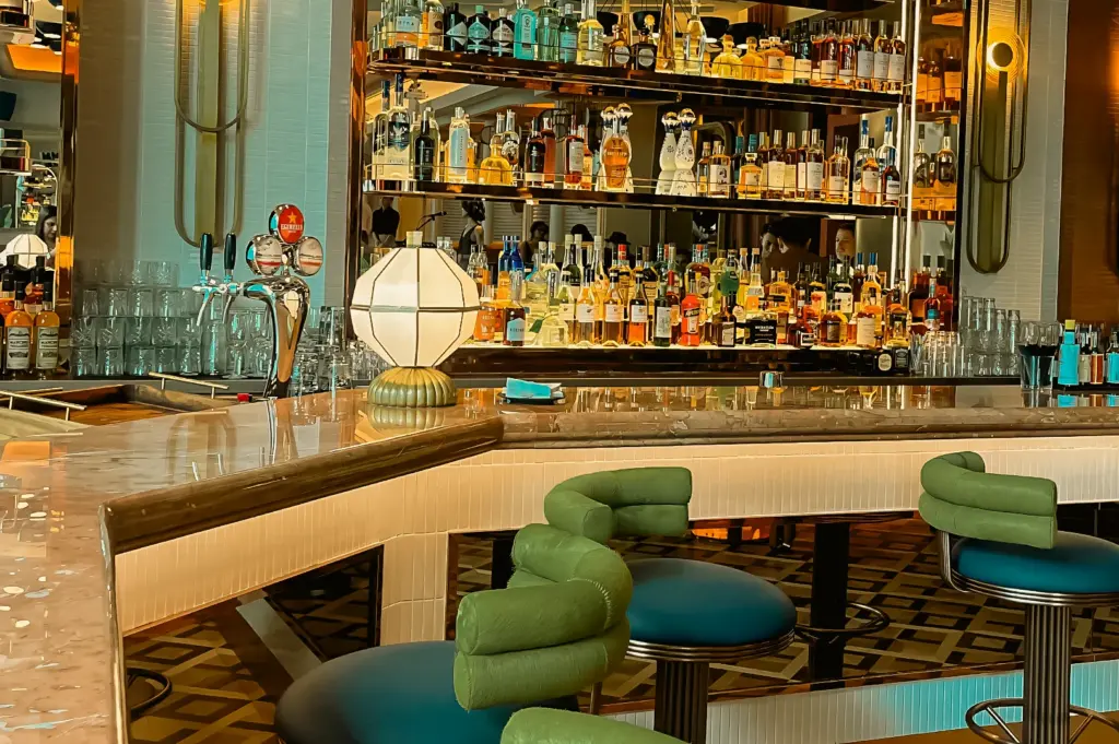 Slight low-angle wide shot of The Whisper Room Singapore cocktail bar with fully stocked backlit shelves, premium spirits, and stylish seating in a vibrant nightlife lounge