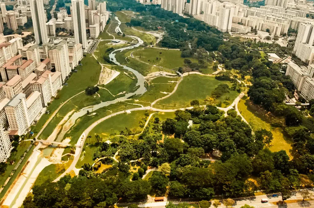 Aerial drone shot of Bishan-Ang Mo Kio Park with winding river and surrounding HDB flats in Singapore, showcasing green spaces near popular dining areas and neighborhood food spots