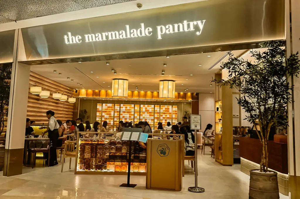 The Marmalade Pantry restaurant interior with diners and glowing shelves, bathed in warm ambient ceiling lighting and soft diffused illumination, captured in a wide-angle eye-level shot.