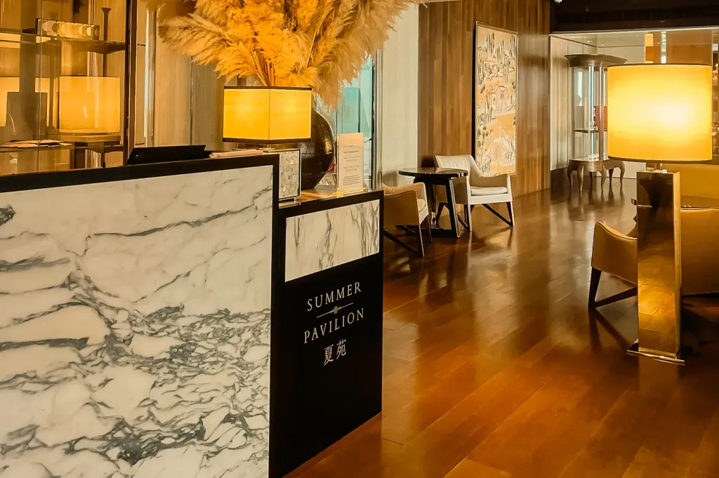 Modern restaurant reception area with marble counter and wooden flooring accented by decorative lamps, illuminated by warm soft ambient lighting and accent glow, captured in a wide-angle eye-level shot.