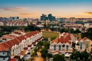 A high-angle, wide panoramic shot of the residential landscape in the Serangoon neighborhood, Singapore, showcasing rows of landed houses with distinct red-tiled roofs, surrounding green lawns, and modern high-rise buildings standing against a dramatic orange and blue sunset sky.