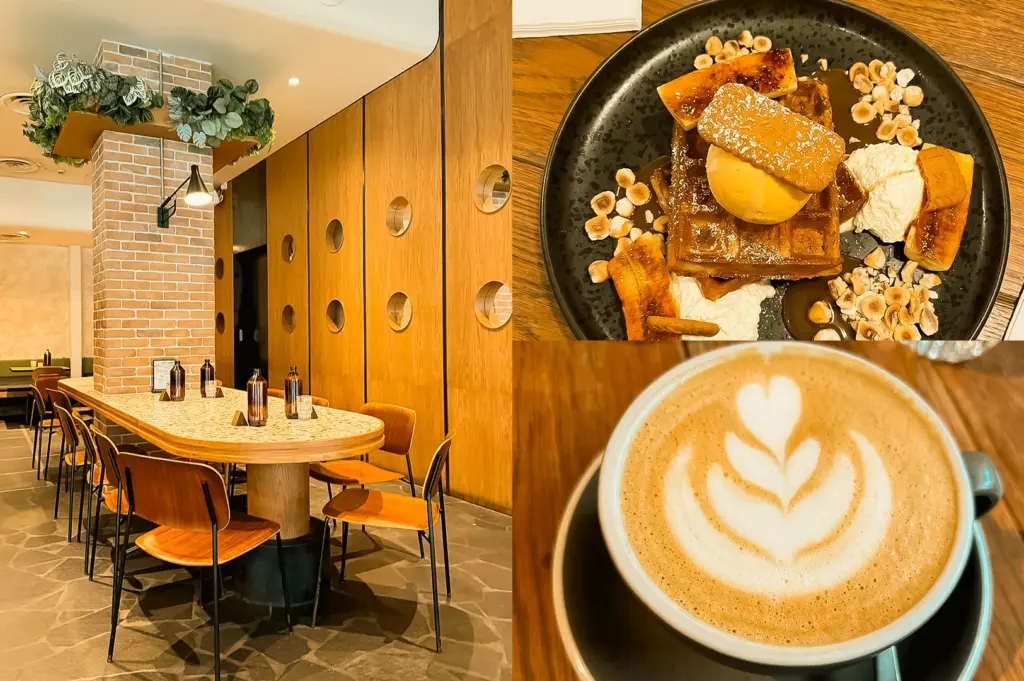 Left: wide-angle eye-level shot of a modern café interior with a long marble-top communal table, wooden chairs, warm ambient lighting, a brick column, and a wood-paneled wall with circular cutouts, accented by indoor greenery and pendant lights; Upper Right: top-down close-up of a plated waffle dessert on a black ceramic dish with sliced bananas, nuts, syrup, cream, and a scoop of ice cream on a wooden table; Lower Right: close-up eye-level shot of a latte in a ceramic cup featuring leaf-shaped latte art, set on a saucer with soft warm lighting and a blurred café background.