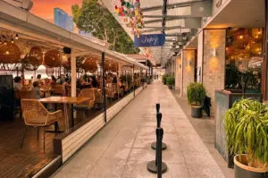Wide-angle eye-level shot of Jypsy One Fullerton alfresco dining area in Singapore, featuring waterfront seating, warm sunset lighting, and couples enjoying a romantic Marina Bay restaurant experience.