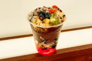 Close-up slightly top-down shot of a fresh acai bowl in a clear cup topped with strawberries, blueberries, kiwi, dragon fruit, granola, and coconut flakes, perfect healthy snack before heading home