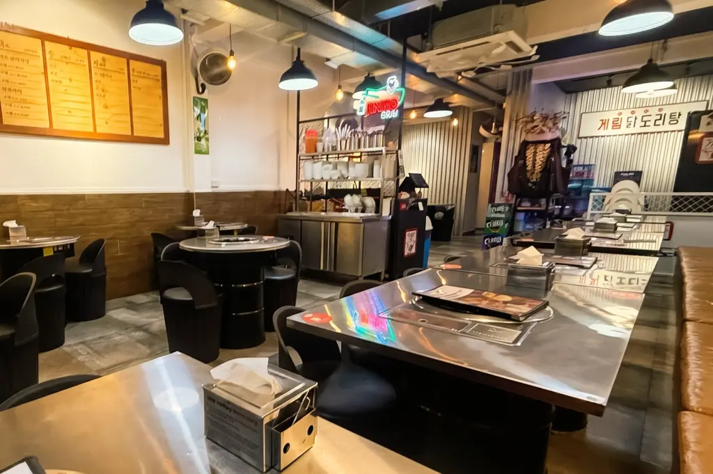 Interior of Kelim Dakdoritang Korean restaurant in Serangoon Garden, wide-angle view of casual communal dining space with metal tables, overhead lighting, and open Korean kitchen setup for shared hot pot meals