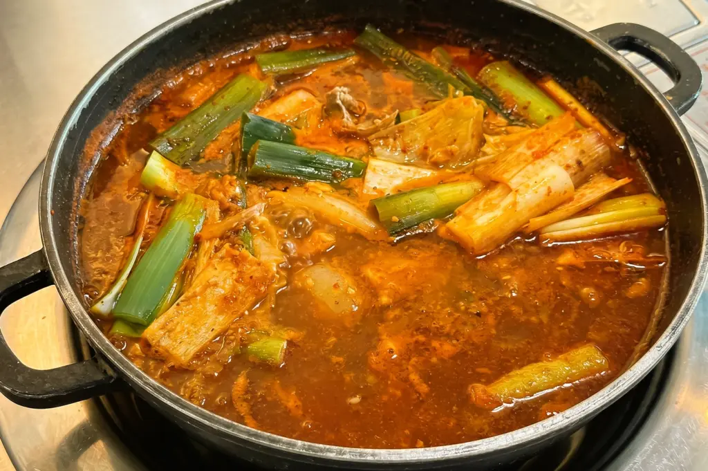 Close-up high-angle view of dakdoritang Korean spicy chicken stew in a pot with red garlic-rich broth, green onions, kimchi, and tender chicken, highlighting a signature Korean comfort dish in Singapore