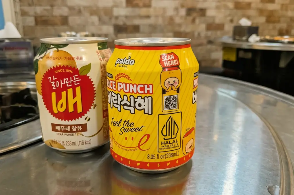 Close-up eye-level shot of Korean canned drinks including Paldo rice punch and pear juice on a metal table at Kelim Dakdoritang restaurant, highlighting refreshing beverages paired with spicy Korean chicken stew in Singapore