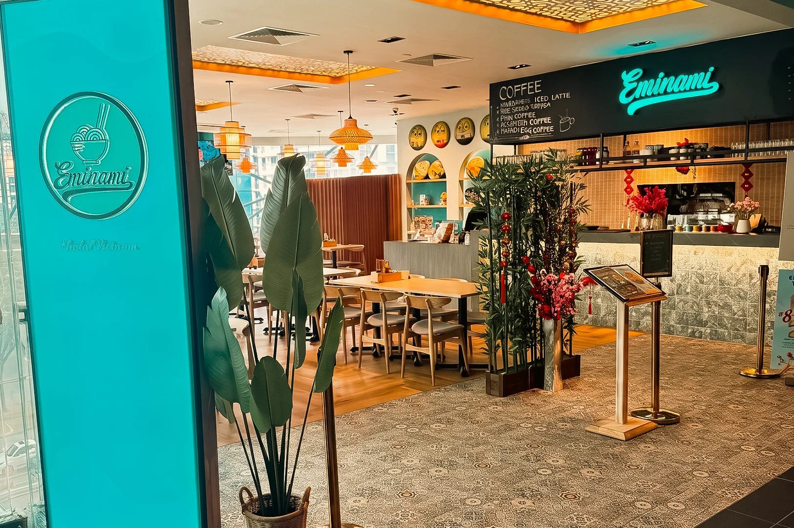 Wide-angle entrance shot of Eminami Vietnamese restaurant at Downtown East Pasir Ris, showcasing the welcoming café entrance, modern Vietnamese-inspired interior, cozy dining area, warm ambient lighting, and signature Eminami branding.