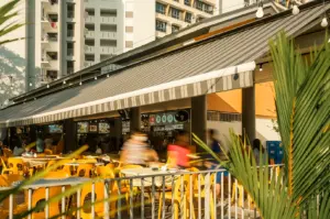 Wide-angle eye-level exterior view of Kimly Coffee Shop at Pasir Ris, featuring outdoor seating, vibrant yellow chairs, and a bustling 24-hour neighbourhood dining atmosphere in Singapore.