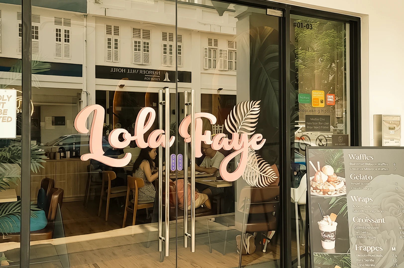 Eye-level front-facing shot of Lola Faye Cafe's storefront on Geylang Road, Singapore, featuring the cafe's signature branding, glass entrance, cozy dining space, and welcoming neighborhood cafe atmosphere.