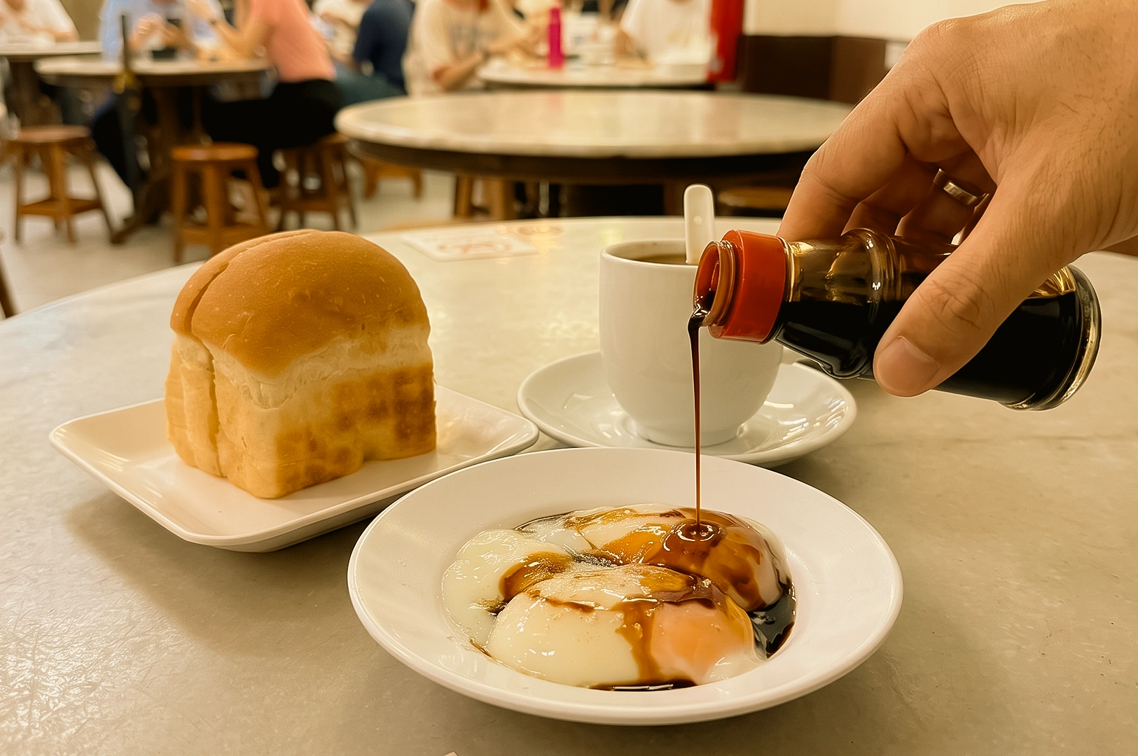 Low-angle close-up of a traditional Singapore breakfast at a Beach Road kopitiam, featuring soft-boiled eggs topped with soy sauce, kaya toast, and kopi coffee on a marble table.