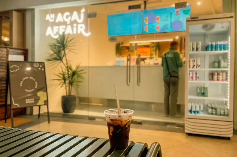 Low-angle eye-level view of an iced drink on a bench outside An Acai Affair at Robertson Quay, Singapore, capturing a quiet after-work pause, café culture, and the comfort of returning to a familiar acai shop. [The Day I...Back Here | Word]