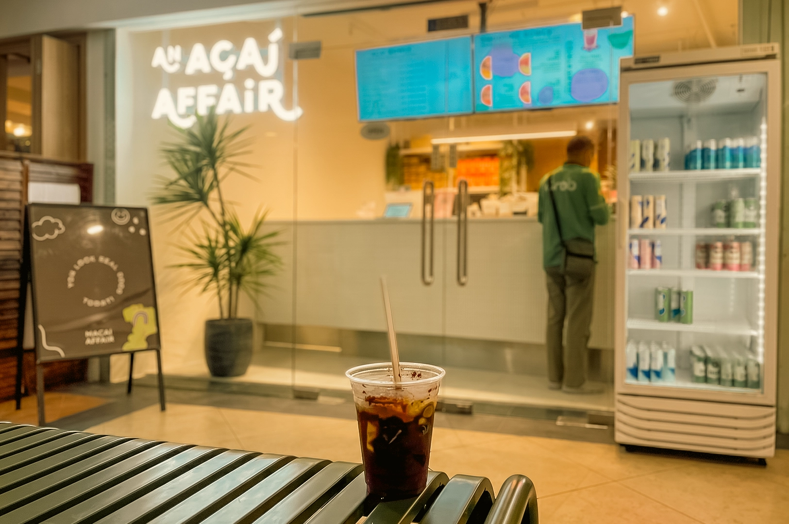 Low-angle eye-level view of an iced drink on a bench outside An Acai Affair at Robertson Quay, Singapore, capturing a quiet after-work pause, café culture, and the comfort of returning to a familiar acai shop. [The Day I...Back Here | Word]