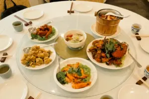 Overhead view of a shared Chinese seafood dinner at a family table in Marine Parade Singapore, featuring Gan Xiang crab, sauna prawns, clam bee hoon, salted egg sotong and Champagne pork ribs served family-style on a traditional lazy Susan.