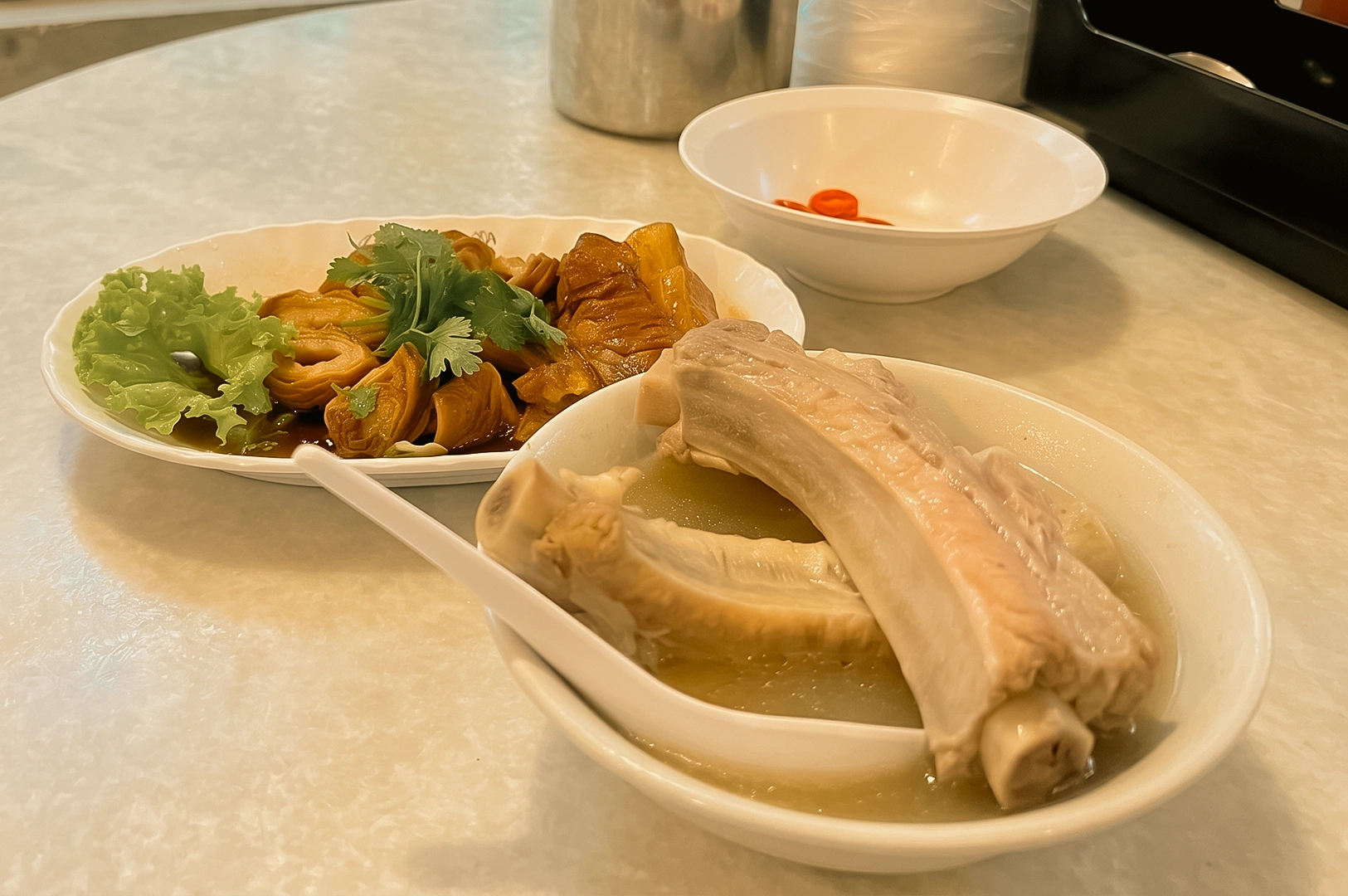 Eye-level dining table view featuring pork rib soup, braised side dishes and rice at a local Singapore eatery, capturing a meaningful food-sharing experience.