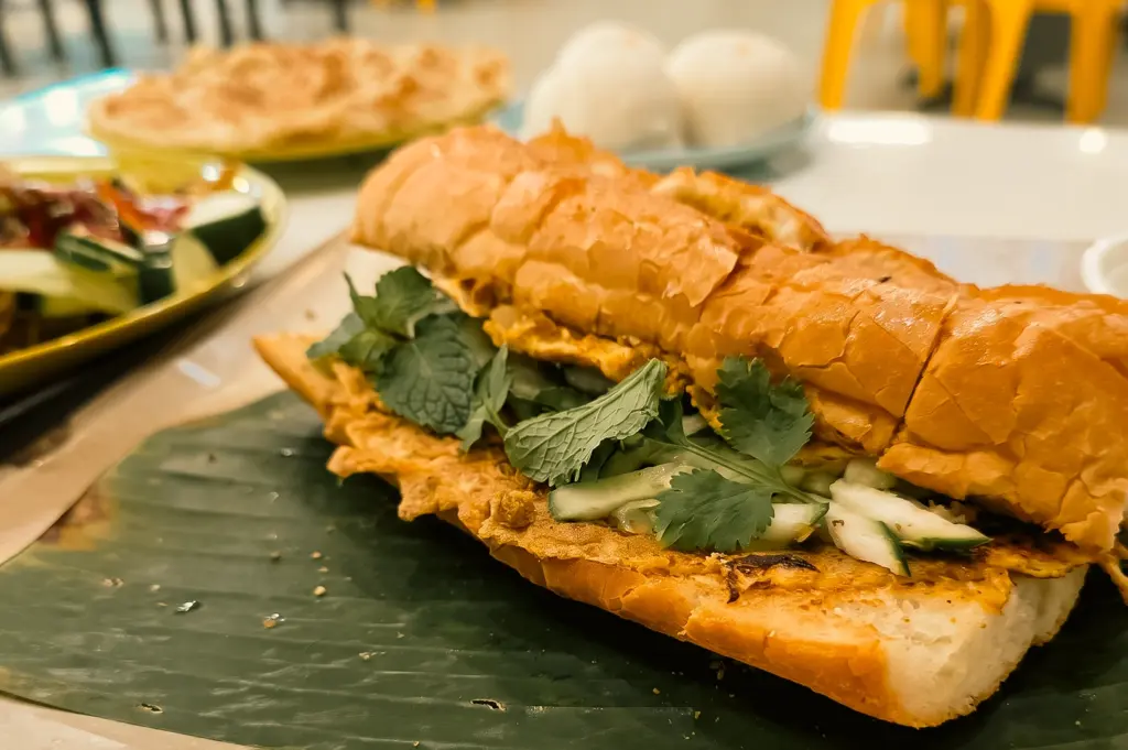 ow-angle close-up of Roti John from King Omar at Kimly Coffee Shop Pasir Ris, featuring a toasted bread roll filled with egg, fresh cucumber, herbs, and savoury flavours popular in Singapore's coffeeshop scene.