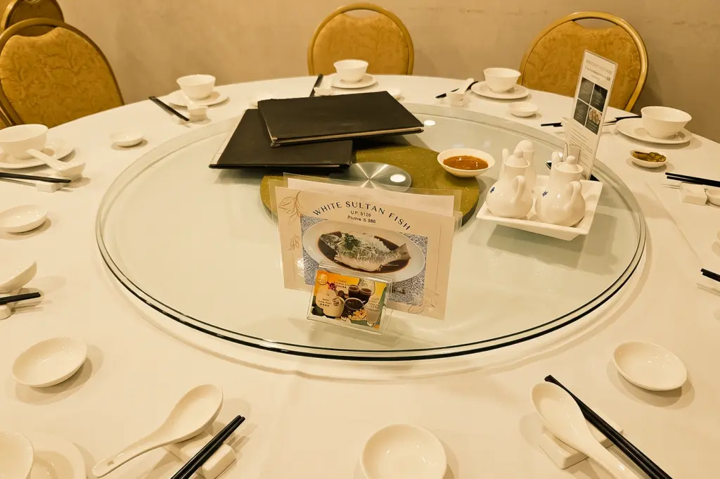 Front-facing wide-angle shot of a large round Chinese banquet table with a glass lazy Susan, elegant tableware, and menu displays at Diamond Kitchen, showcasing a family-friendly Chinese dining experience in Marine Parade, Singapore.