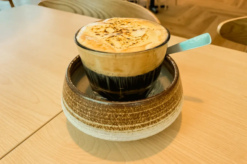 Close-up tabletop shot of a traditional Vietnamese egg coffee at Eminami, featuring creamy torched foam, rich dark coffee, artisan ceramic serving bowl, and inviting café ambiance.