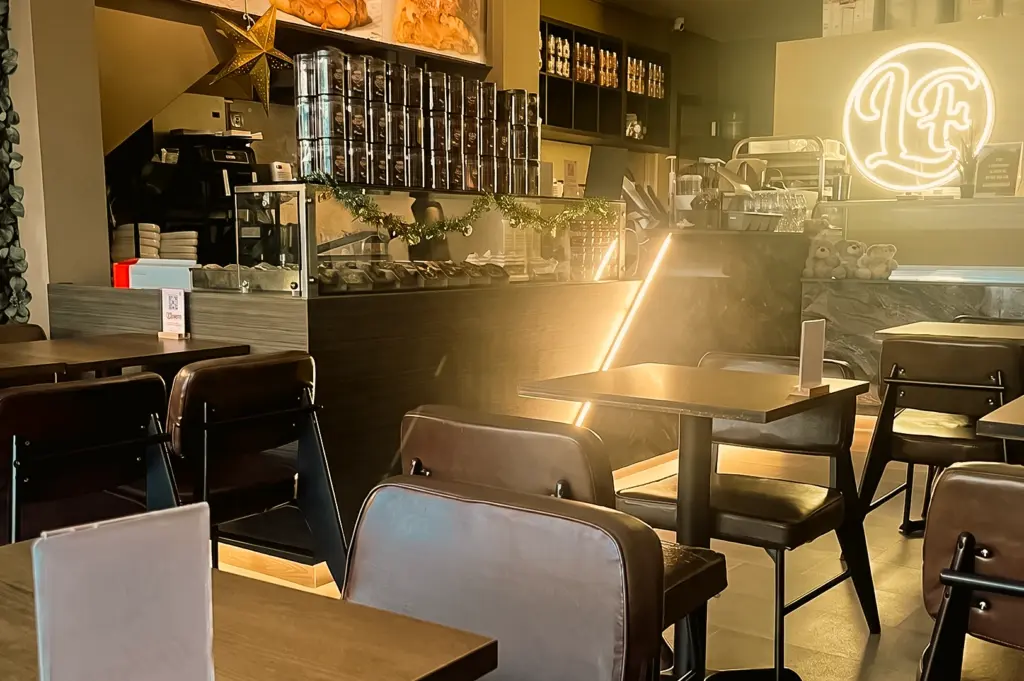 Wide-angle eye-level shot of Lola Faye Cafe's warm modern interior on Geylang Road, Singapore, featuring cozy seating, ambient lighting, specialty coffee counter, and inviting late-night cafe atmosphere.