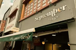 Storefront cafe entrance of September Coffee with white signage on a grey shophouse façade and a green awning reading "coffee, space, & friends".