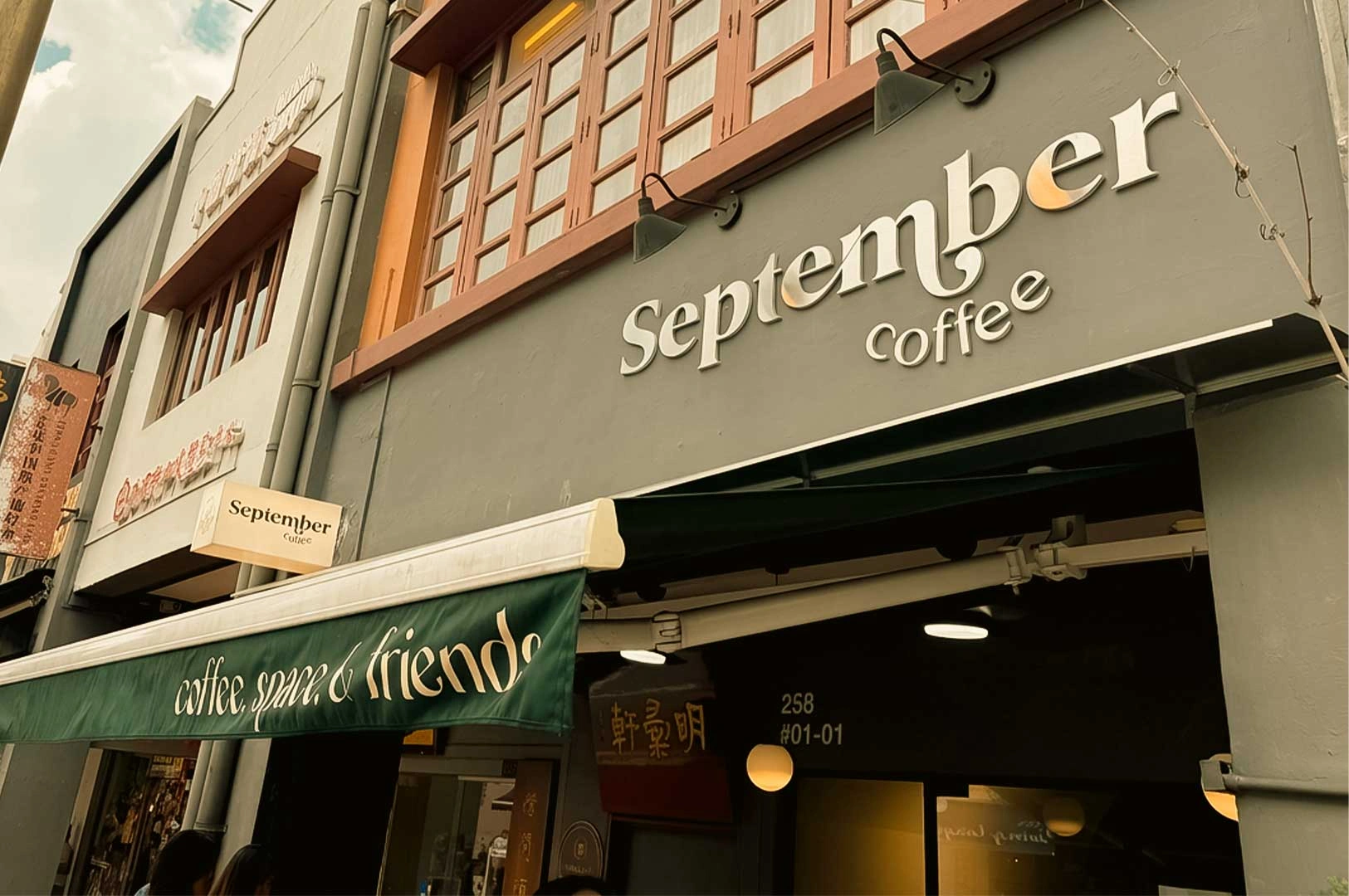 Storefront cafe entrance of September Coffee with white signage on a grey shophouse façade and a green awning reading "coffee, space, & friends".