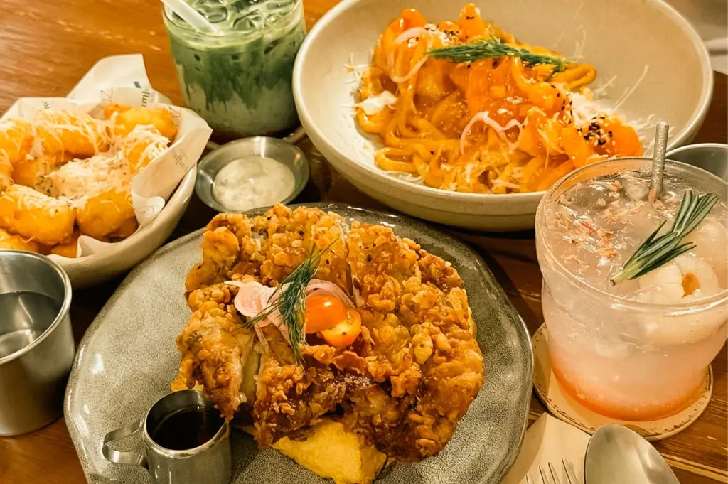Flat lay of cafe dishes at September Coffee including fried chicken waffle, creamy pasta, tater tots, an iced matcha latte, and a lychee drink.